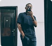 Saviour Inyang in a dark T-shirt, taking a mirror photo beside a door